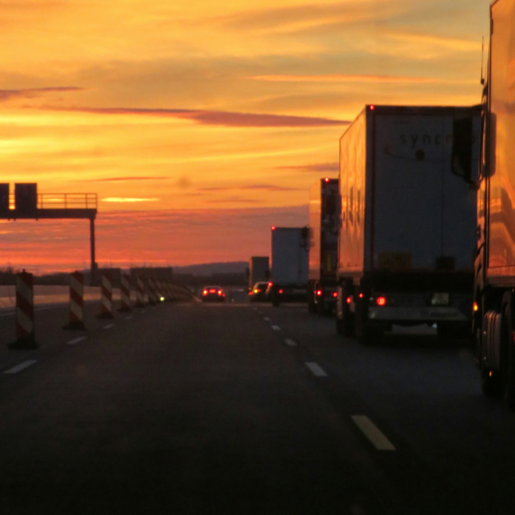 LKW und PKW auf einer deutschen Autobahn im Sonnenuntergang, Absperrbaken am Seitenstreifen