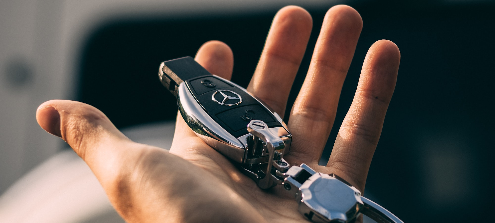 Eine geöffnete Handfläche hält einen Autoschlüssel vor einem Fahrzeug